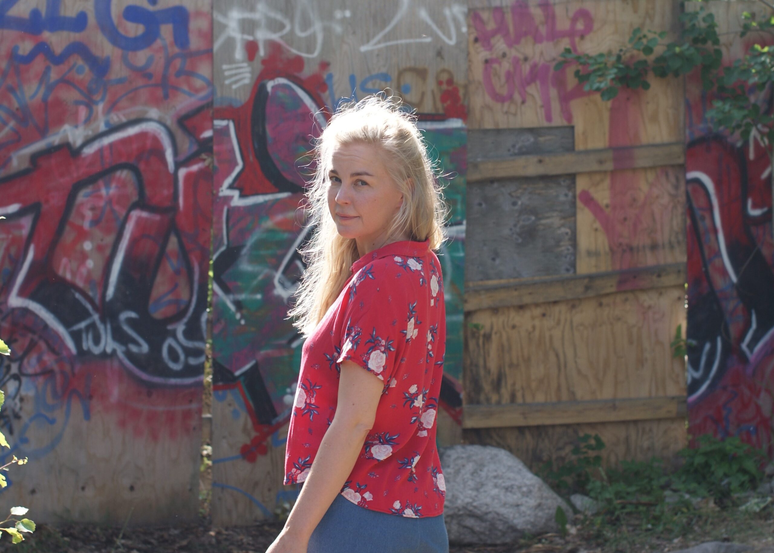 Kääntäjä Minnamari Sinisalo seisoo graffittiaidan edessä ja katsoo kameraan.